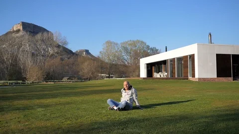 Villa in the mountains. Bald middle-aged man sitting on the lawn and talking Stock Footage 129608739