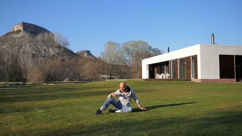 Villa in the mountains. Bald middle-aged man sitting on the lawn and talking Stock Footage 129792800