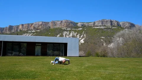 Villa in the mountains. Middle-aged man doing workout on the grass. Capoeirajump Stock Footage 129731546