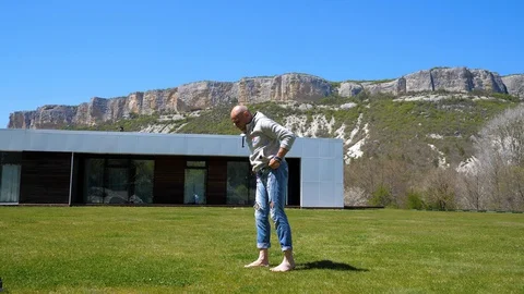 Villa in mountains. Middle-aged man does warming up on the grass. Capoeirajump Stock Footage 129731570