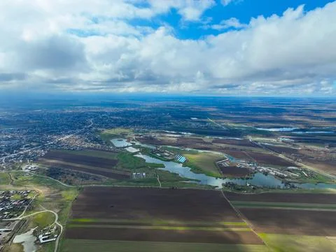 Village and fields bordered by small interconnected lakes under cloudy sky Stock Photos