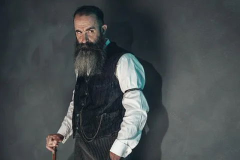 Vintage beard man in 1900 style fashion with cane against grey wall. Stock Photos