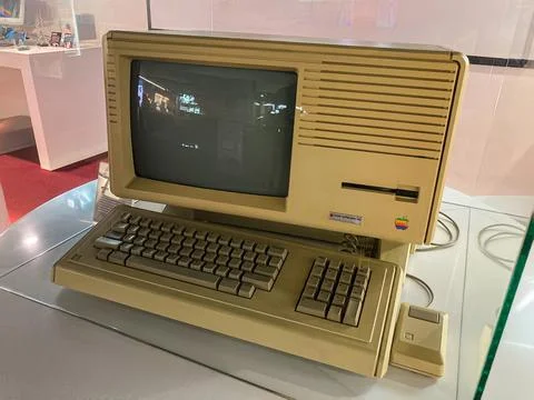 A vintage beige personal computer on display in a museum, with indistinct scr Stock Photos