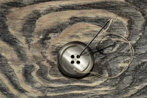 Vintage button with needle and thread on the aged textured boards Stock Photos