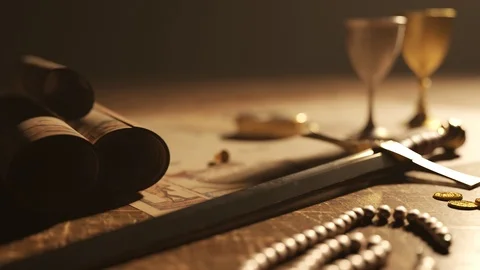 The vintage compass on the ancient map next to the sword, goblets and jewels. Video stock 102665351
