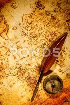 Vintage compass and goose quill pen lying on an old map. Stock Photos