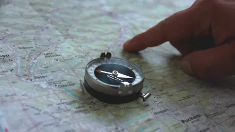 Vintage compass on a mountain map with man's hand finger searching for a trail Stock Footage 248785173