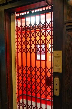 A vintage elevator with a red, expandable gate stands open invitingly. Stock Photos