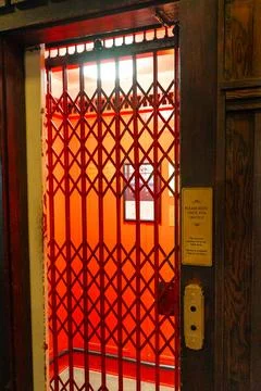 A vintage elevator with a red scissor gate and 'buzz for service' sign. Stock Photos