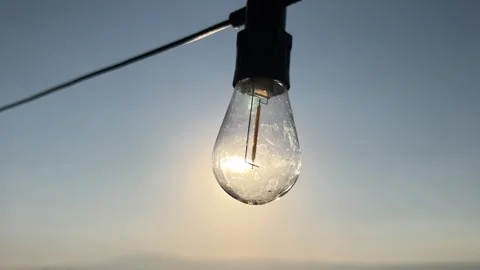 Vintage Hanging Light Bulb with Sun Flare and Sunset Background 4K Stock Footage 345026356