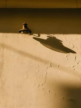 Vintage lamp casting long shadows across weathered wall, golden sunlight Stock Photos