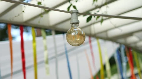 Vintage light bulb hanging under a canopy with colorful ribbons in the back.. Stock Footage 284525587
