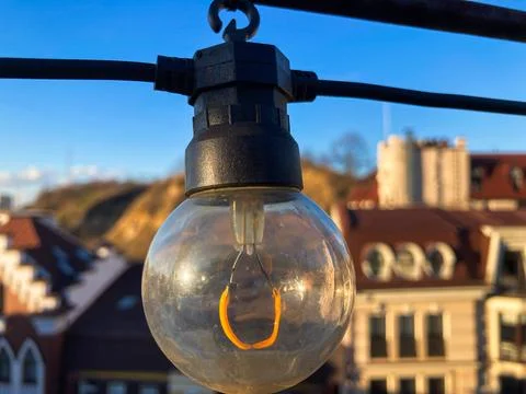 A vintage light bulb hangs from a bracket or hook in an urban setting, poss.. Stock Photos