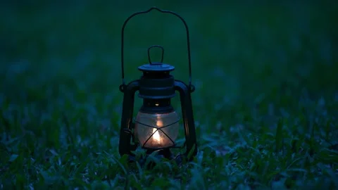 Vintage old lantern lighting in the dark forest. Travel camping concept.  Burning lantern on a moss at forest in the night. Stock Photo