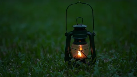 Vintage old lantern lighting in the dark forest. Travel camping concept.  Burning lantern on a moss at forest in the night. Stock Photo