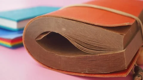 Vintage orange notebook bound with elastic band on pink background with oth.. Stock Footage 332263218