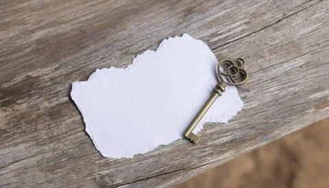 Vintage Skeleton Key with Blank Torn Paper on Rustic Wooden Background Stock Photos