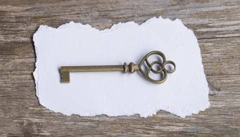 Vintage Skeleton Key on Blank Torn Paper over Rustic Wooden Background Stock Photos