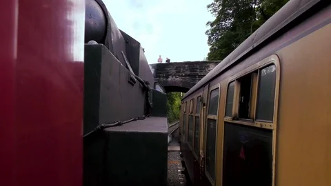 Vintage steam train producing smoke passing under countryside bridge Stock Footage 80307930