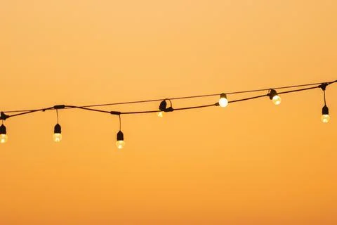 Vintage warm light bulbs on string wire at sunset. Stock Photos