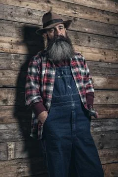 Vintage worker man with long gray beard in jeans dungarees. Standing in front Stock Photos