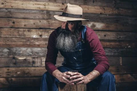 Vintage worker man with long gray beard in jeans dungarees holding whiskey. S Stock Photos
