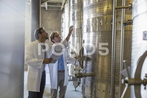 Vintners in lab coats checking vats in winery cellar Stock Photos