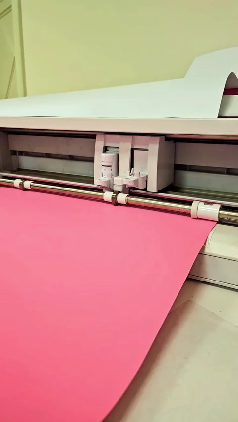 Vinyl cutting plotter machine feeding a roll of pink vinyl film Stock Footage 346134629