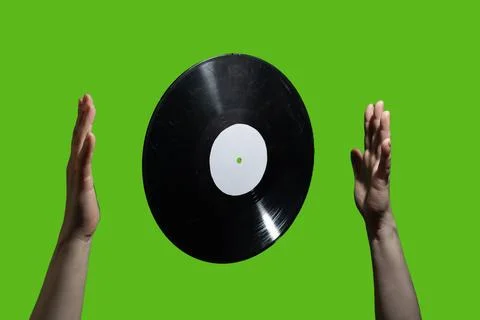 A vinyl record elegantly floating between two hands against a vibrant green Stock Photos