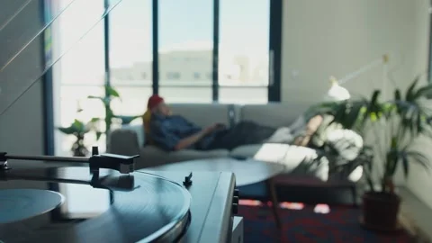 Vinyl record player spinning while man relaxes on sofa Stock Footage 307603060