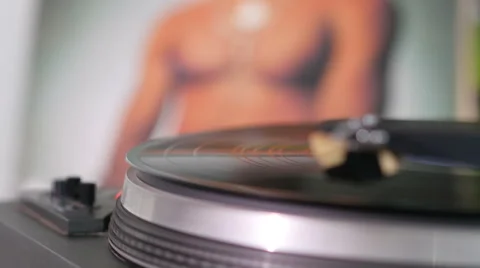 Vinyl record spinning on turntable. Record sleeve with male torso in background. Stock Footage 50606502
