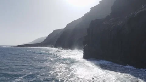Violent white waves smash dark volcanic cliffs, creating dramatic white foam Stock Footage 308420403
