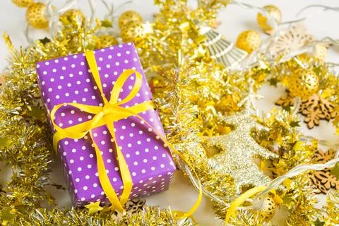 Violet elegant present with yellow ribbon on golden tinsesl and garland Stock Photos