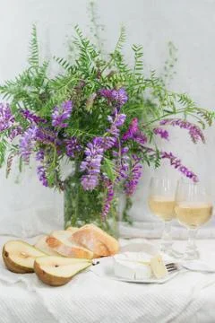 Violet flowers, pears, brie cheese and wine glasses. Still life Stock Photos
