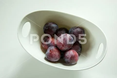 Violet plums in a white bowl on a white background Stock Photos