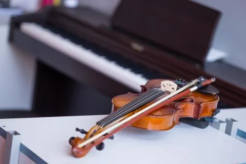 Violin and bow on table with blured brown piano in background Stock Photos
