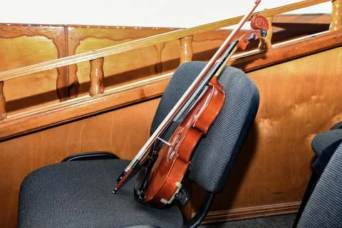A violin with a bow and notes stands on a chair in the middle of an empty con Photos