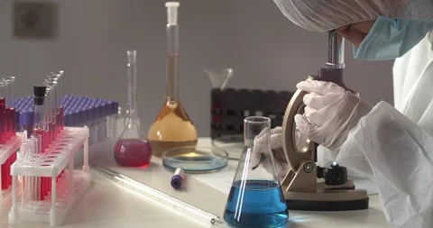 Virologist in a protective suit doing experiments in a lab, using microscope Video stock 129717733
