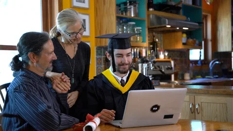 Virtual commencement ceremon with young man in graduation costume sits in front Video stock 128986622