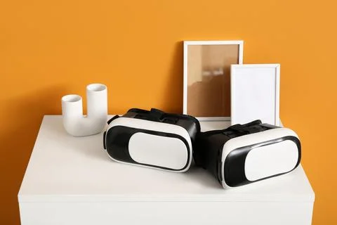 Virtual reality headsets on white table with picture frames and vase, modern  Stock Photos