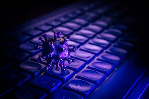Virus model placed on a computer keyboard, illuminated with blue and purple.. Stock Photos