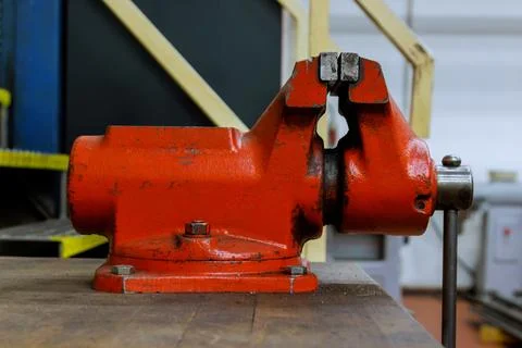 The vise is fixed on the metalworking workbench. Red vice on a wooden table Stock Photos