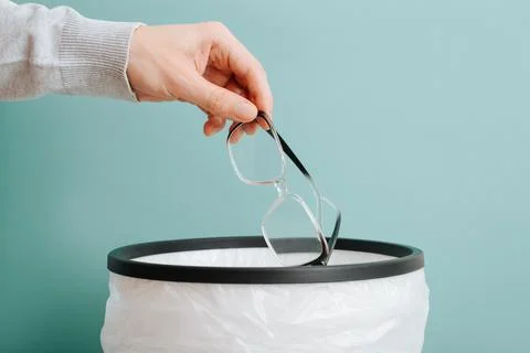 Vision correction concept. Close-up of hand throwing out eyeglasses into tr.. Stock Photos