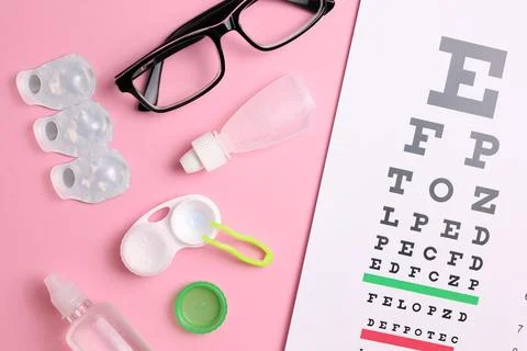 Vision test table, glasses and contact lenses on a colored background. Stock Photos