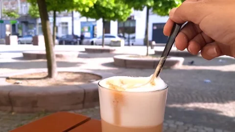 Visitor in cafe stirs sugar with spoon in glass of latte coffee. Stock Footage 277363493