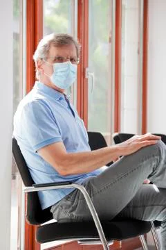 Visitor or patient sitting in an empty waiting room with face mask because of 写真素材