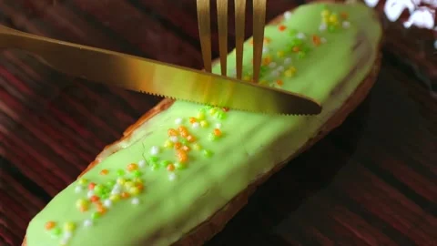 Visitor slices eclair pastry glaze cover with knife and fork Stock Footage 277790069