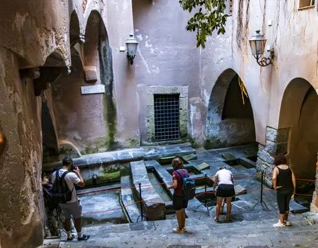 Visitors descend worn stone steps into the shaded medieval washhouse Stock Photos
