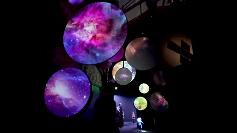 Visitors explore a dim gallery of hanging circular screens projecting microbes Vidéo 331193624