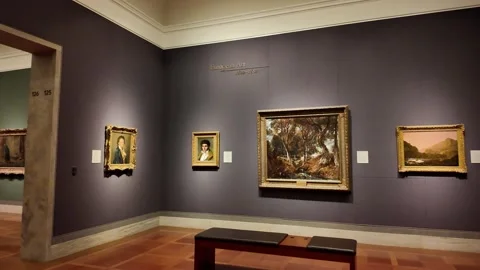 Visitors explore a gallery filled with golden framed paintings and silver art. 库存影片 333917634